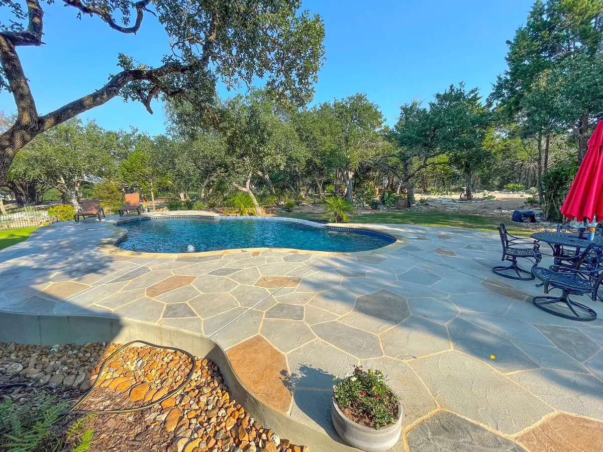 Freeform pool surrounded by a stone terrace and mature trees